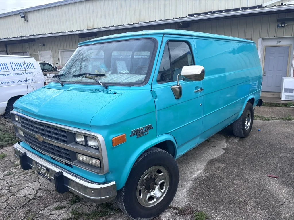 A bright turquoise vintage Chevrolet van parked outside a workshop